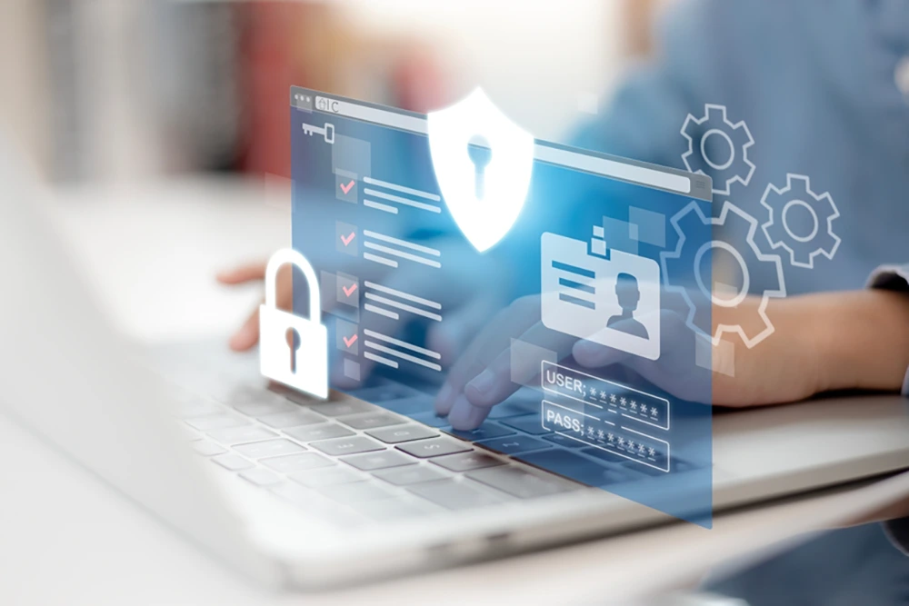 Ein Benutzer tippt auf einem Laptop, während ein digitales Interface mit Login-Feldern, einem Schutzschild, Zahnrädern und einem Vorhängeschloss als Projektion angezeigt wird.