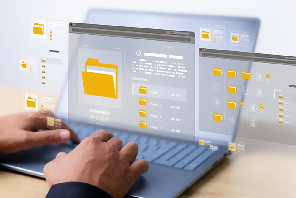 Zwei Hände bedienen einen Laptop, auf dessen Bildschirm mehrere digitale Benutzeroberflächen mit gelben Ordnersymbolen und Dateiinformationen eingeblendet sind.