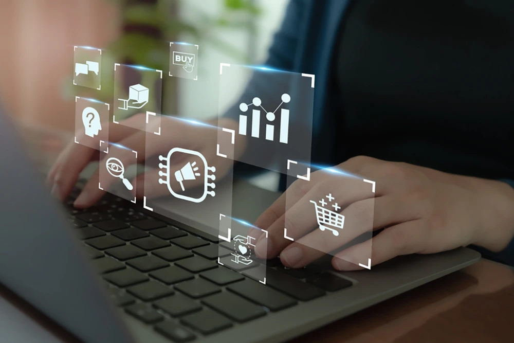 Hände tippen auf einem Laptop, während über dem Gerät verschiedene digitale Symbole schweben, darunter ein Einkaufswagen, ein Diagramm, eine Lupe, ein Megafon und ein Prozessor-Chip. Die Darstellung steht für ERP-Software und Datenanalyse.