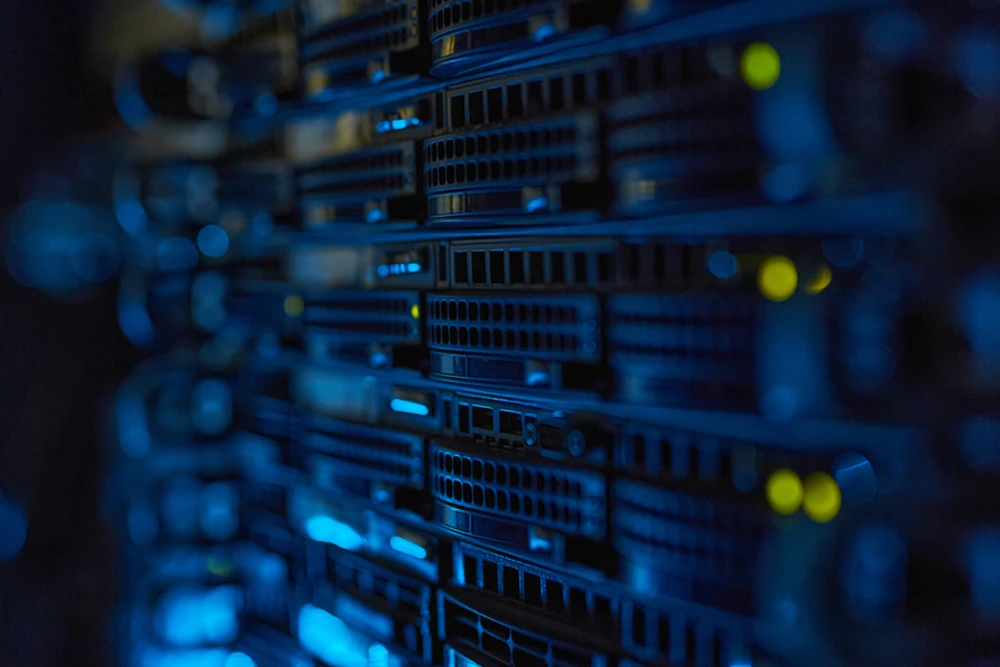 Nahaufnahme mehrerer Serverracks mit aktiver Hardware in einem Rechenzentrum. Die Geräte leuchten in Blau mit gelben Status-LEDs.